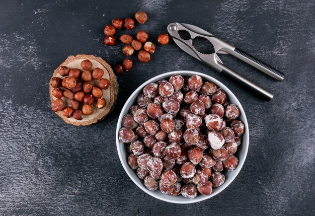 Noisettes décortiquées dans un bol blanc avec morceau de bois vue de dessus sur une table en pierre sombre