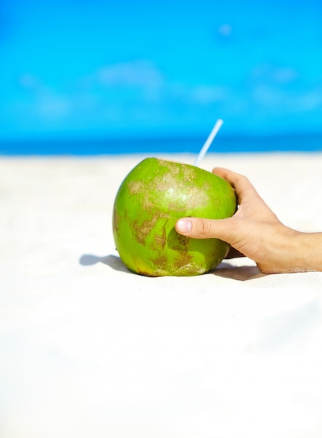 Noix de coco avec la main sur la plage blanche