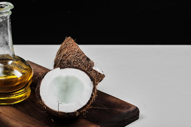 Photo gratuite noix de coco à moitié coupée et bouteille d'huile sur planche de bois.