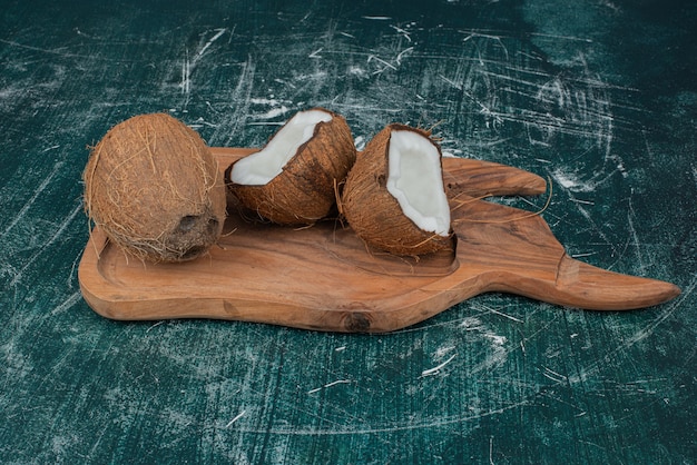 Photo gratuite noix de coco à moitié coupées et entières sur planche de bois.