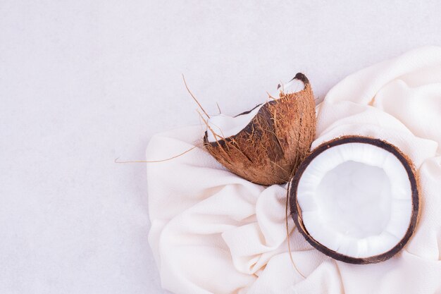 Noix de coco poilue cassée en deux sur une nappe blanche.