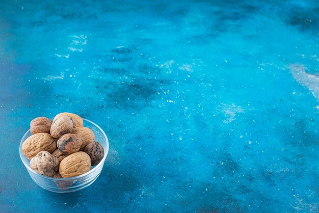 Noix en coque dans un bol en verre sur la surface bleue