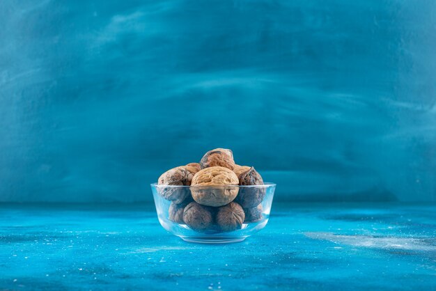 Noix en coque dans un bol en verre , sur la table bleue.