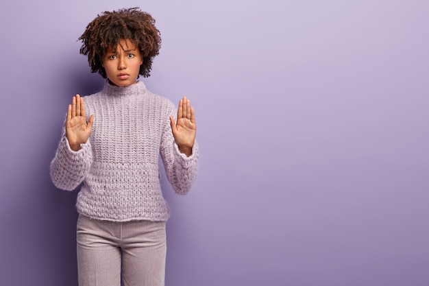 Photo gratuite non, je refuse. belle femme à la peau sombre en colère montre des paumes, fait un geste d'arrêt avec les deux mains, exprime son désaccord, porte un pull décontracté, se dresse sur un mur violet, copie l'espace à droite