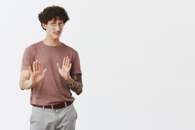 Non, je refuse. Portrait de beau mec mécontent et intense avec bras tatoué de cheveux noirs bouclés et moustache tirant les paumes en retenant et arrêtez le geste en fronçant les sourcils en rejetant les mauvais conseils ou offres