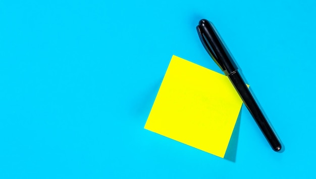 Photo gratuite note jaune avec une place vide pour le texte avec un marqueur sur fond bleu à plat