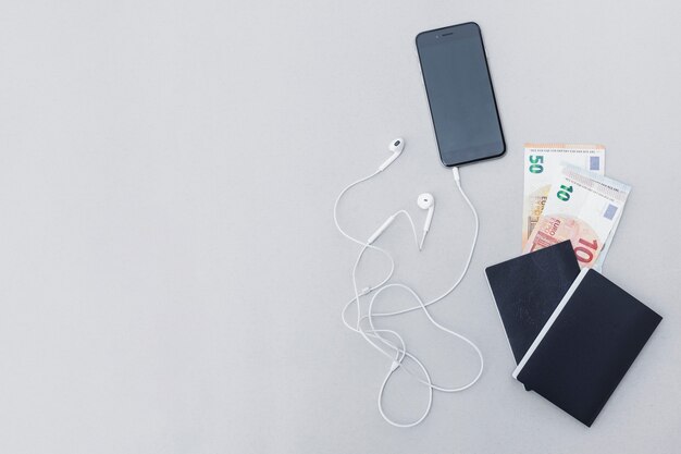 Note de monnaie dans le passeport avec téléphone portable et écouteur sur fond gris