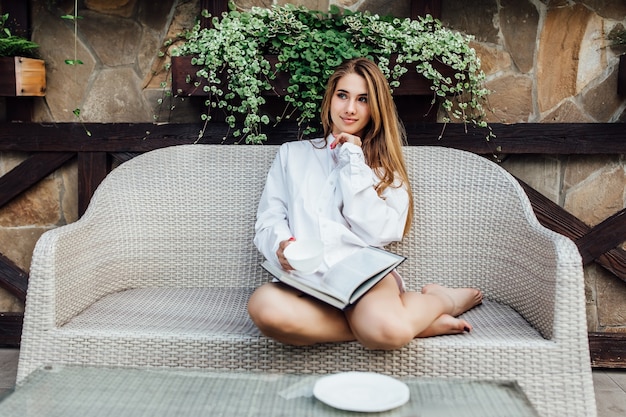 Notion du matin. Superbe et jolie femme lisant un livre assis sur un canapé et se relaxant avec une tasse de café.