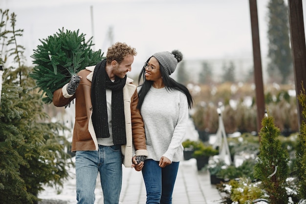 Notion d'hiver. Mec en manteau marron. Vendeur d'arbre de Noël. Couple international.