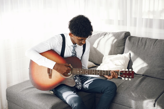 Notion de Hoobies. Jeune homme indien en collants assis dans le salon. Musicien jouant de la guitare.