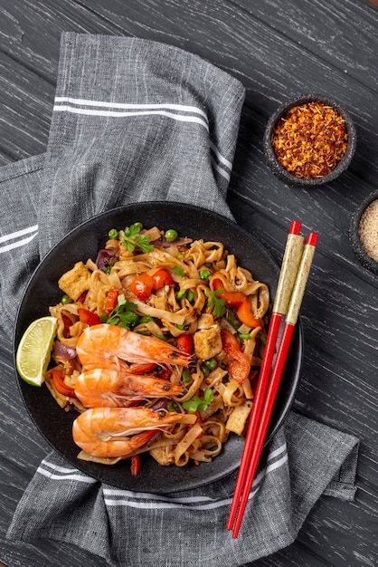 Nouilles plates avec légumes et poulet avec des baguettes et des épices