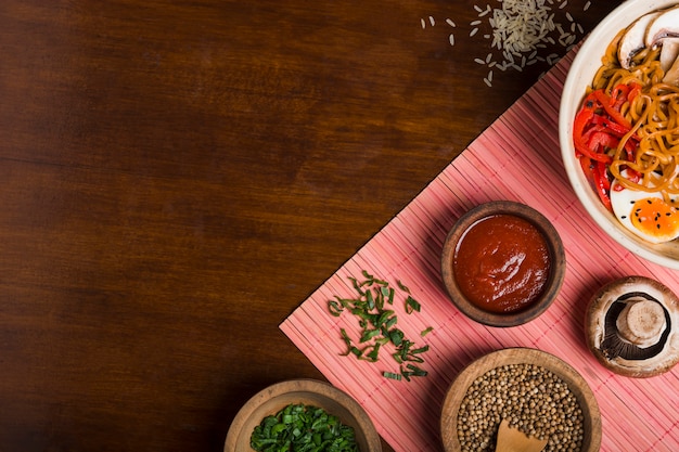 Nouilles Ramen de style asiatique avec des sauces; ciboulette et graines de coriandre sur napperon au-dessus de la table en bois