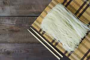 Photo gratuite nouilles de riz cru en place tapis et baguettes sur la table altérée