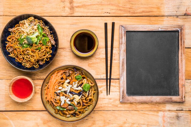 Nouilles thaïlandaises traditionnelles avec sauce; baguettes et ardoise sur le bureau en bois