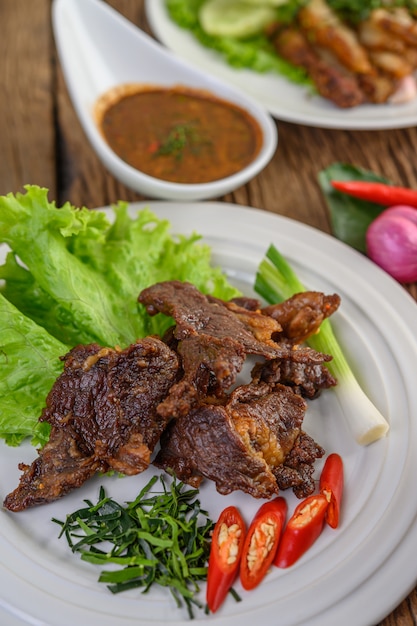 Nourriture thaïe au boeuf frit sur une plaque blanche avec oignon de printemps, feuilles de lime kaffir, piments, salade et pâte de piment dans une tasse.