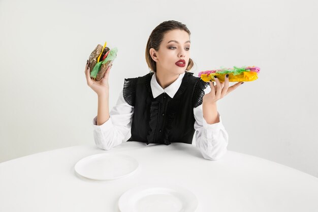 Nous sommes ce que nous mangeons. Une femme mange un hamburger et un hot-dog en plastique, concept écologique. Il y a tellement de polymères que nous en sommes faits. Catastrophe environnementale, mode, beauté, nourriture. Perdre organique.