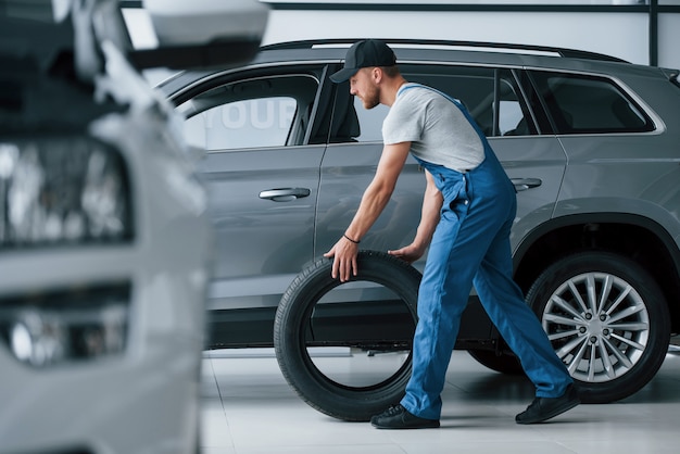 Nouveau. Mécanicien tenant un pneu au garage de réparation. Remplacement des pneus d'hiver et d'été