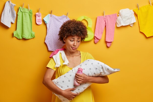 Nouveau-né endormi sur les mains de la mère. Une femme perplexe tient bébé enveloppé dans une serviette, une bouteille de lait, prend soin de son bébé, ne peut pas comprendre pourquoi sa fille pleure, occupée à faire des tâches ménagères