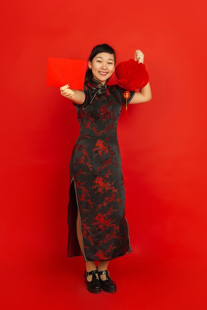 Nouvel an chinois 2020. Portrait de jeune fille asiatique isolé sur fond rouge. Le modèle féminin en vêtements traditionnels a l'air heureux avec la décoration et l'enveloppe rouge. Célébration, vacances, émotions.