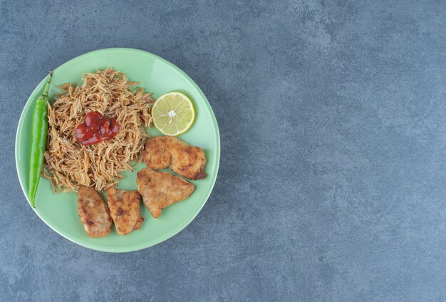 Nuggets de poulet et pâtes frites sur plaque verte.