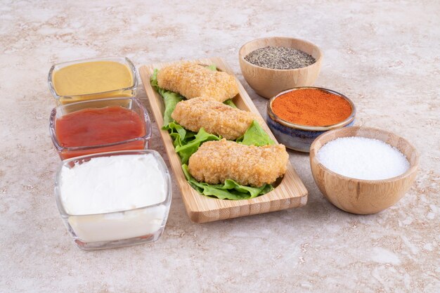 Nuggets de poulet sur une planche en bois avec une variété de sauces autour.