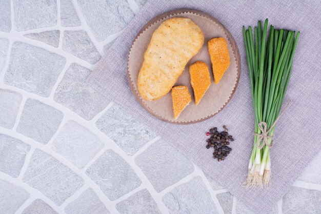 Nuggets de poulet et de poisson sur planche de bois avec un bouquet d'oignon vert.