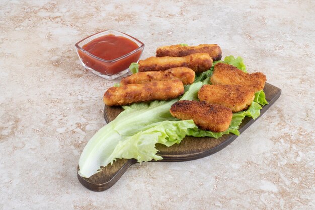 Nuggets de poulet et saucisses frites sur une feuille de laitue verte sur une planche en bois.