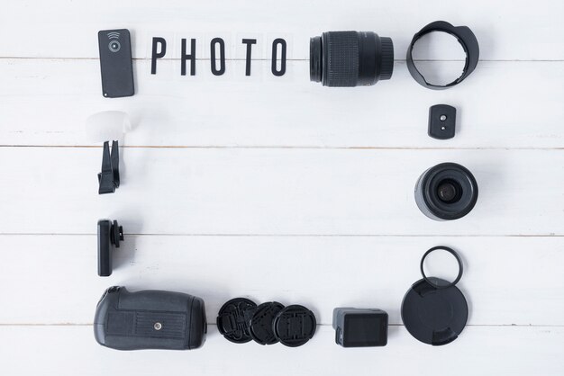 Objectif de la caméra avec accessoires de photographie et texte photo disposé sur une table en bois blanc