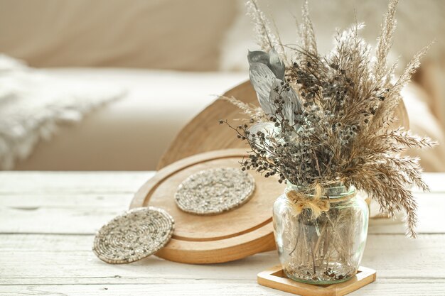 Objets de décoration dans l'intérieur confortable de la pièce, un vase avec des fleurs séchées sur une table en bois clair.