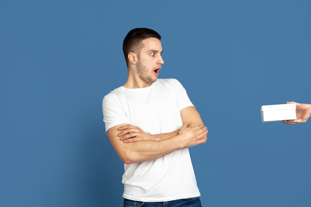 Obtenir un coffret cadeau. Portrait du jeune homme caucasien sur fond bleu.