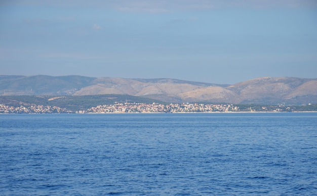 Océan calme avec de l'eau scintillante et une ville côtière et des montagnes à l'horizon