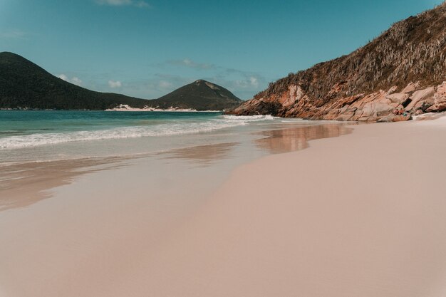 Océan ondulé frappant la plage de sable entourée de montagnes à Rio de Janeiro