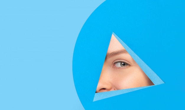Photo gratuite oeil féminin à la recherche, furtivement à travers le triangle en fond bleu