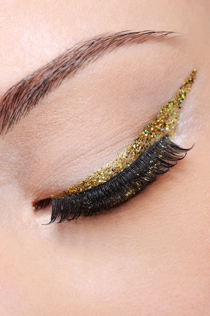 Photo gratuite oeil fermé de l'oeil féminin avec flèche eye-liner doré brillant brillant