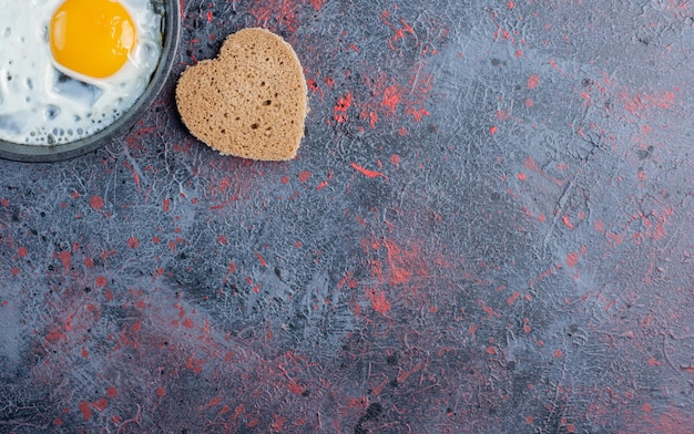 Oeuf au plat dans une casserole avec des tranches de pain en forme de coeur de côté.