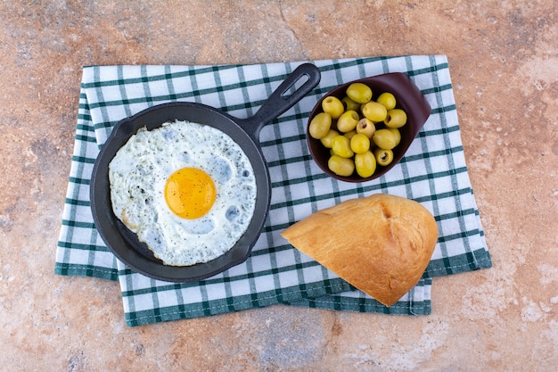 Oeuf au plat dans une poêle servi avec des olives marinées