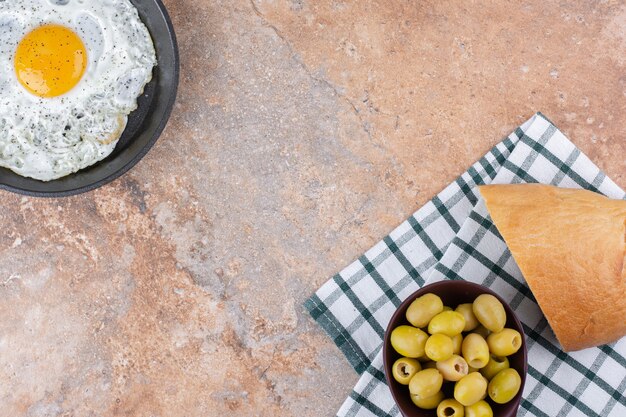 Oeuf au plat dans une poêle servi avec des olives vertes marinées