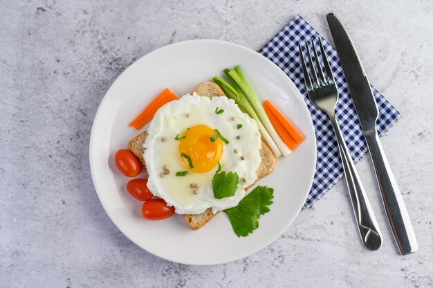 Un œuf au plat portant sur un toast, garni de graines de poivre avec des carottes et des oignons de printemps.