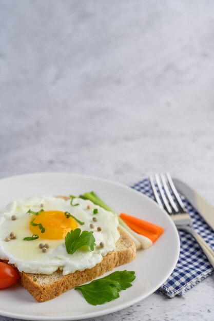 Un œuf au plat portant sur un toast, garni de graines de poivre avec des carottes et des oignons de printemps.