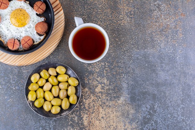 Oeuf au plat avec des saucisses dans une poêle noire avec une tasse de thé