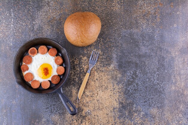 Oeuf au plat avec des saucisses dans une poêle et un petit pain de côté