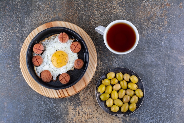 Photo gratuite oeuf au plat avec des saucisses, des olives et une tasse de thé