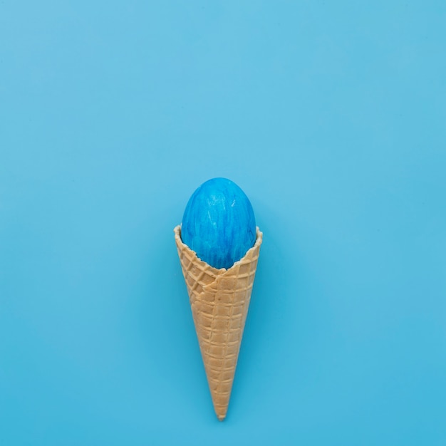 Oeuf bleu en cône de gaufre sur fond bleu