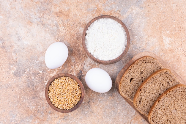 Oeuf, céréales, farine et pain dans une assiette en bois, sur le marbre.