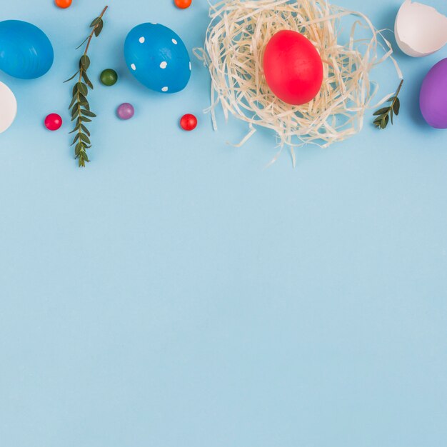 Oeuf coloré dans le nid avec une branche de plante verte et des bonbons