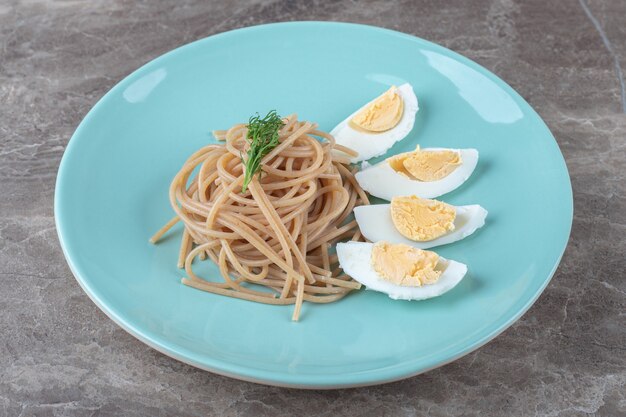 Oeuf à la coque et spaghetti sur plaque bleue.