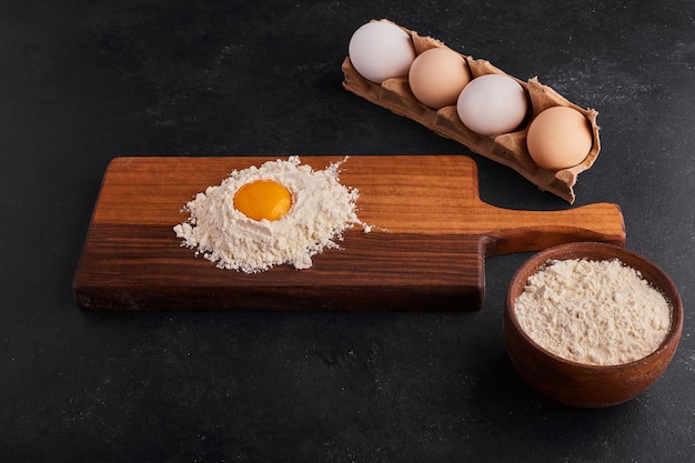 Oeuf et farine mélangés les uns aux autres sur une planche de bois.