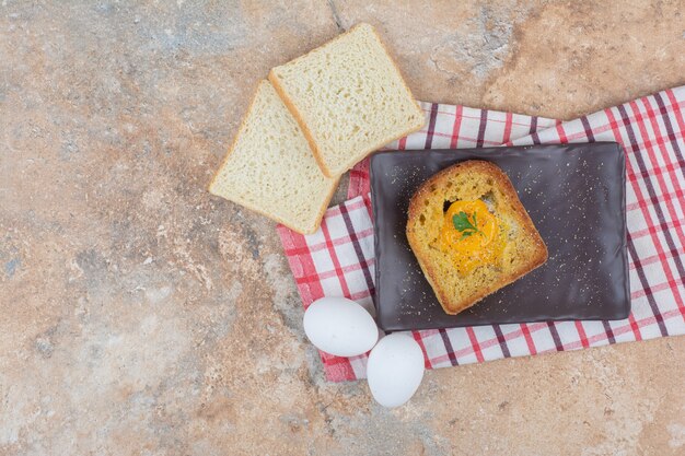 Oeuf frit à l'intérieur du pain grillé sur plaque noire avec des tranches de pain