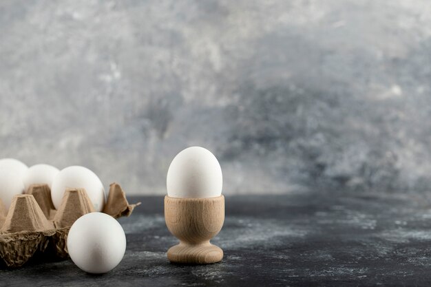 Oeuf de poule cru en coquetier avec boîte à oeufs sur une surface en marbre.