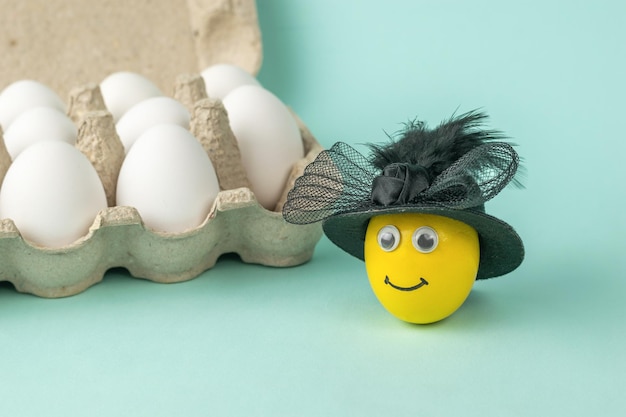 Un œuf avec un visage dans un grand chapeau noir près d'une boîte d'œufs.